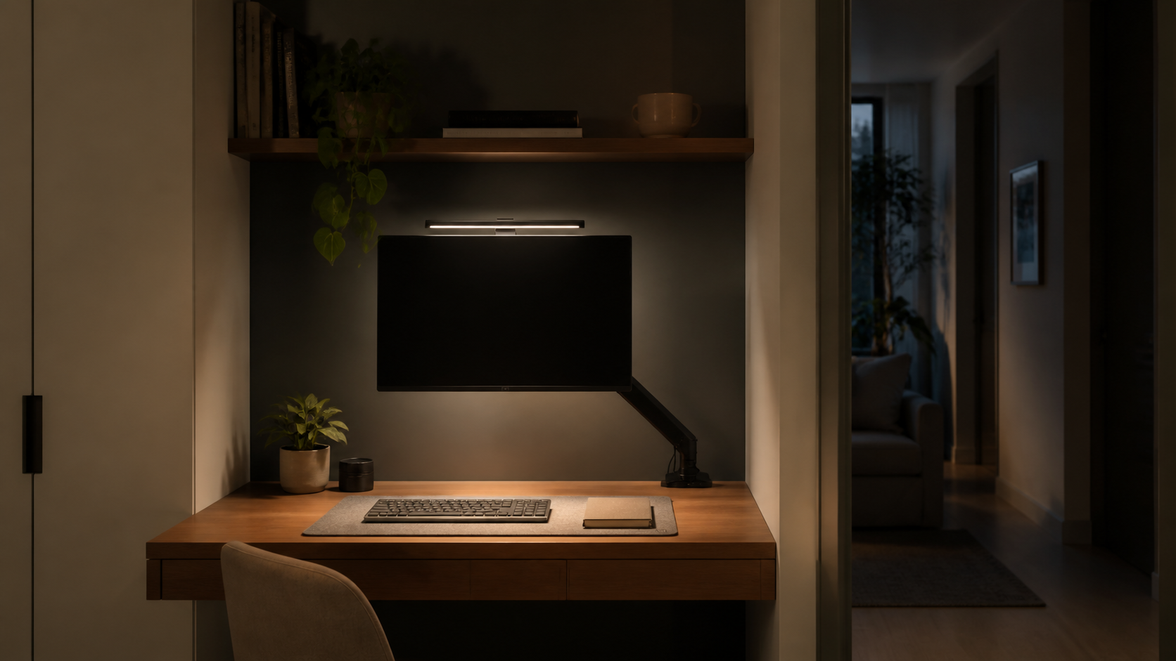 Evening workspace with a slim monitor light bar illuminating the desktop while the adjacent passage remains dim